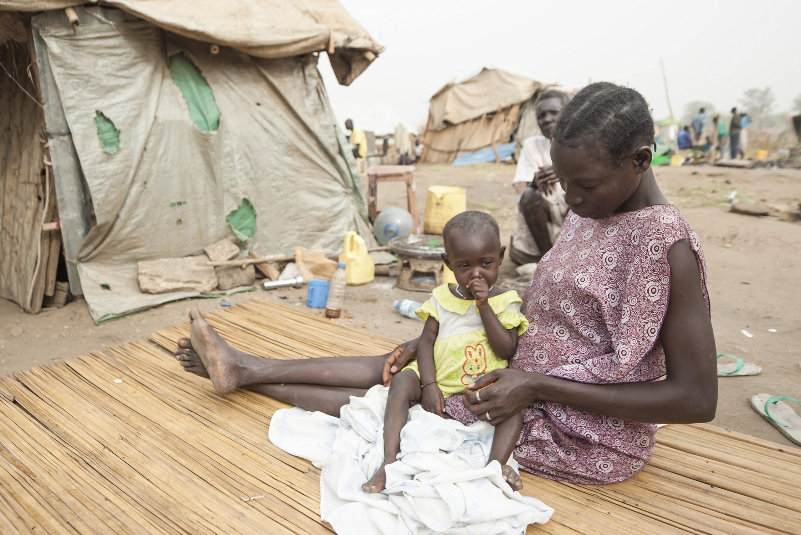 Juba, South Sudan - February 28th, 2012: Unidentified woman sits with her daughter in front of his hovel in displaced persons camp, Juba, South Sudan. Refugees stay in harsh conditions in camps of Juba.